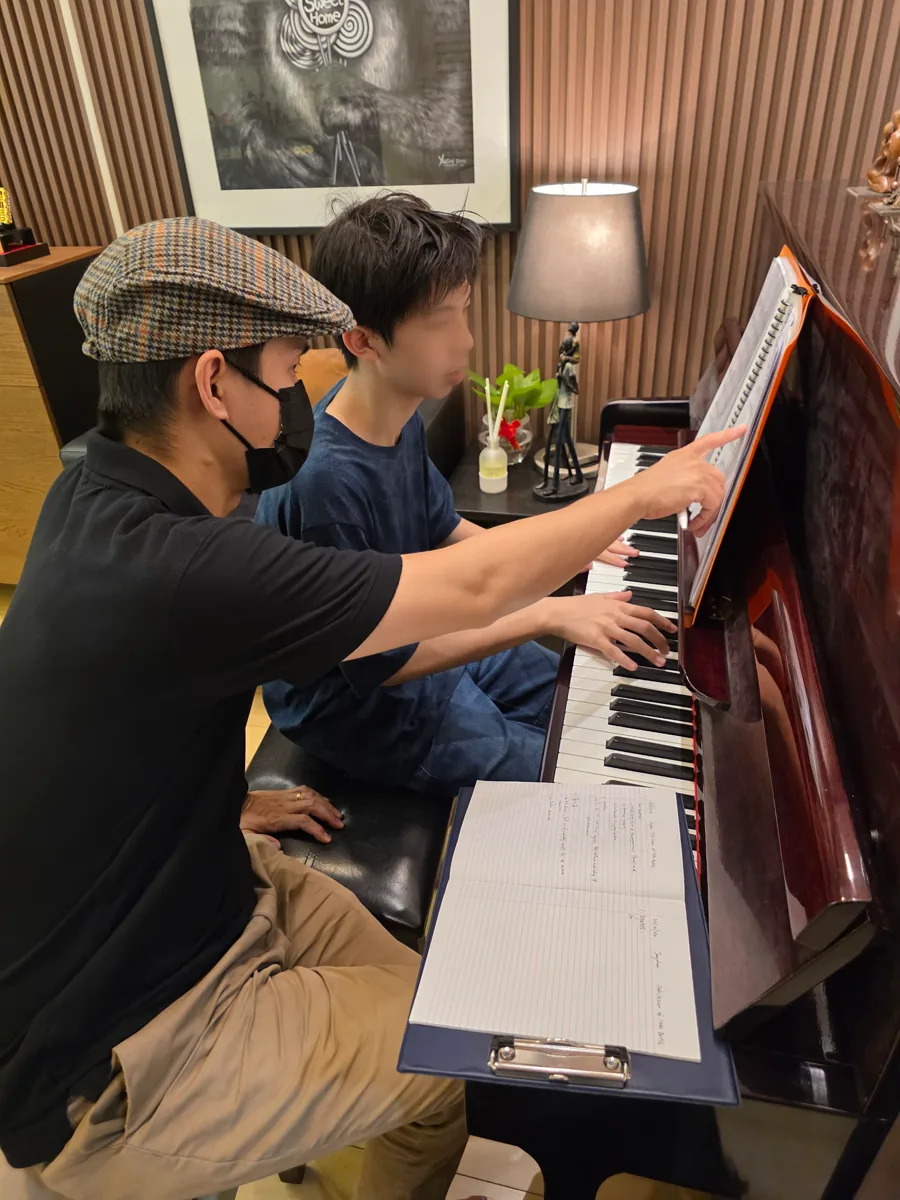 Leroy Lee at an upright piano, pointing at a passage in the score while a teenage student plays.